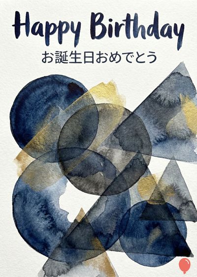 水彩画の誕生日カード。上部に «Happy Birthday» と «お誕生日おめでとう» の文字が書かれている。濃い青、グレー、金色の円と三角形の抽象的なデザインが、白い紙に重なり合っている。右下の小さくて赤い風船のシンボルが描かれている。